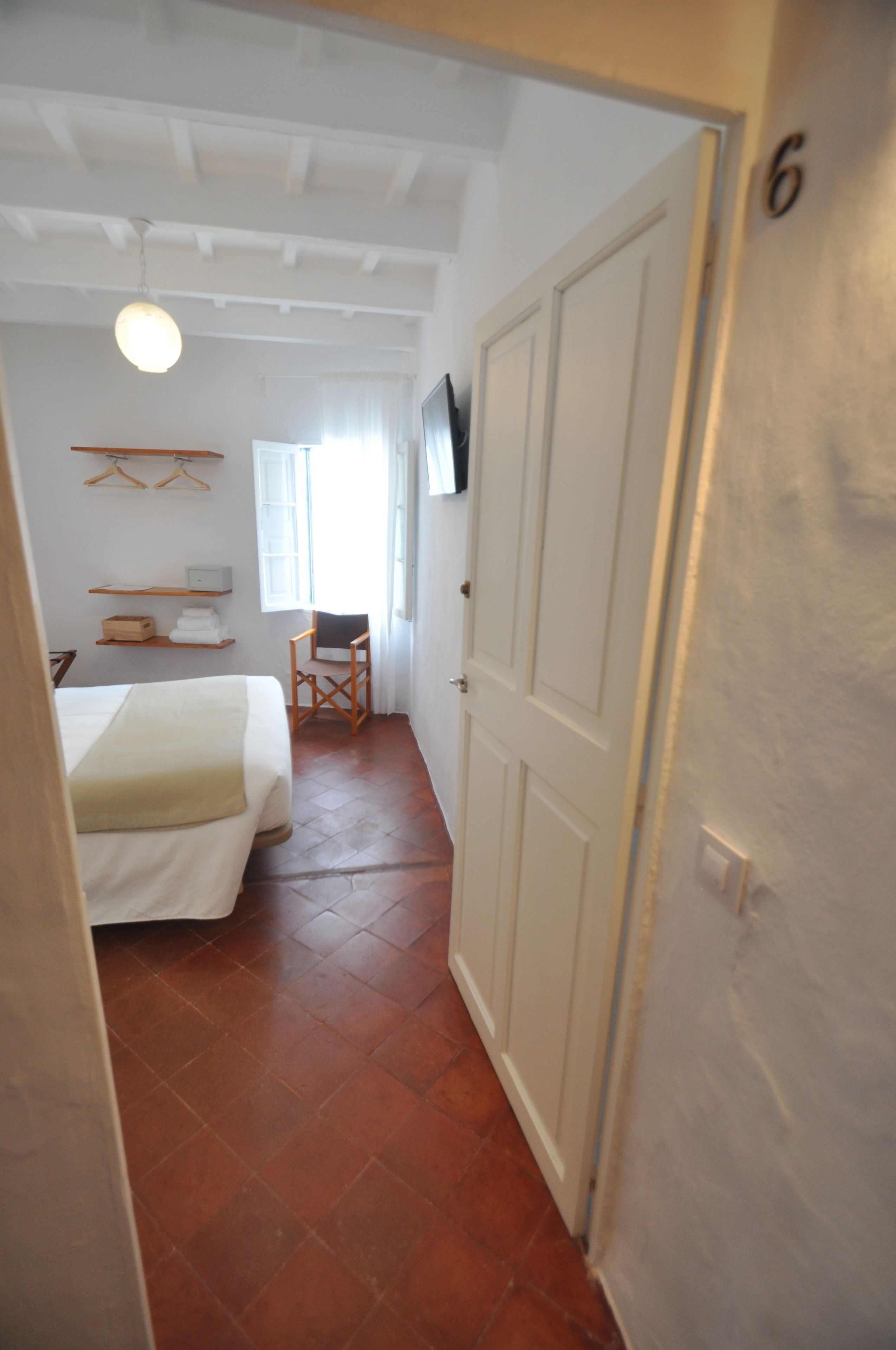 Un pasillo estrecho con una cama, una silla y una puerta con el número 6.
