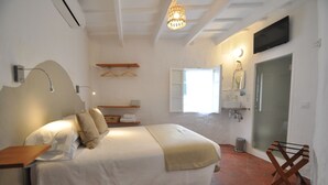 A bedroom with a bed, bedside table, hanging clothes rack, and a bathroom with a sink and mirror. - Port Antic Ciutadella  by My Rooms Hotels (Ciutadella de Menorca)