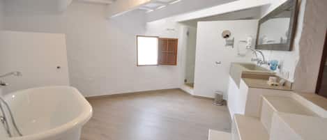 A spacious bathroom with a freestanding bathtub, a large mirror, and a window providing natural light.