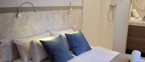 A hotel room with a bed, a bedside table, an air conditioning unit, a shower, and a mirror.