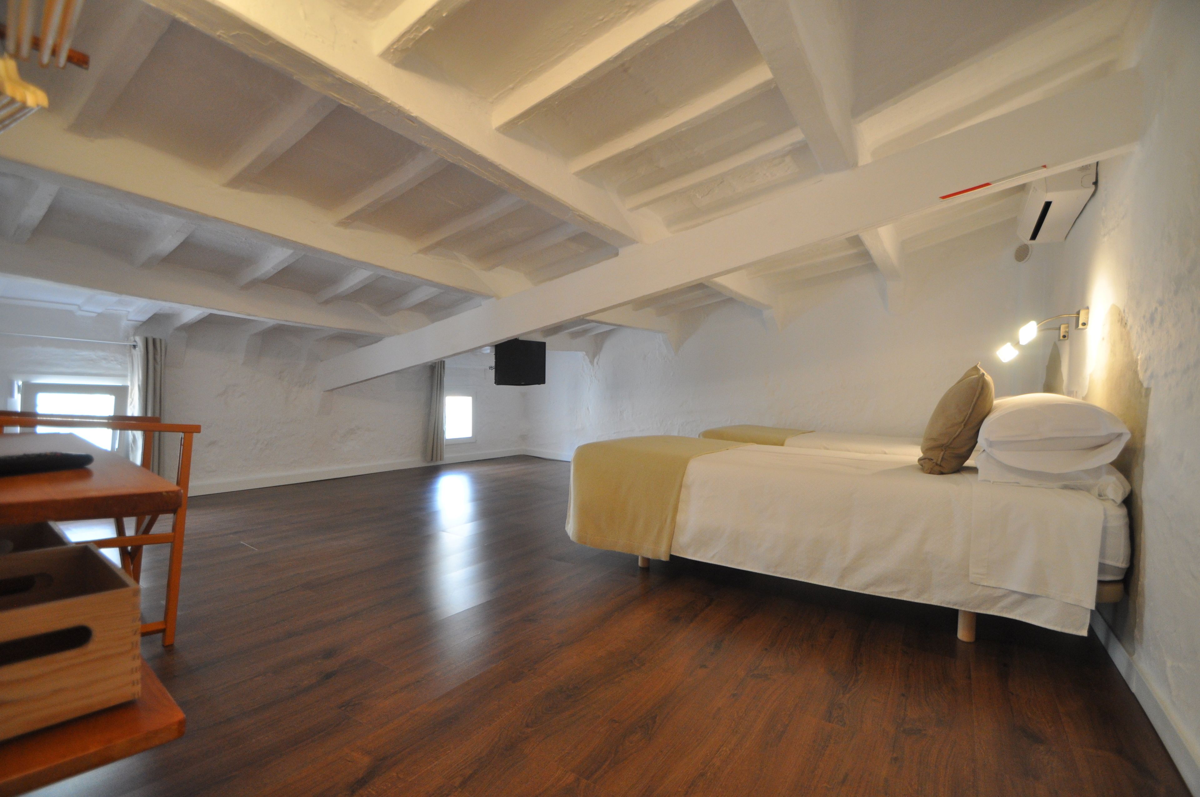 Ein geräumiges Schlafzimmer im Dachgeschoss mit Holzboden, einem Bett mit weißer Bettwäsche und einem Holzstuhl.