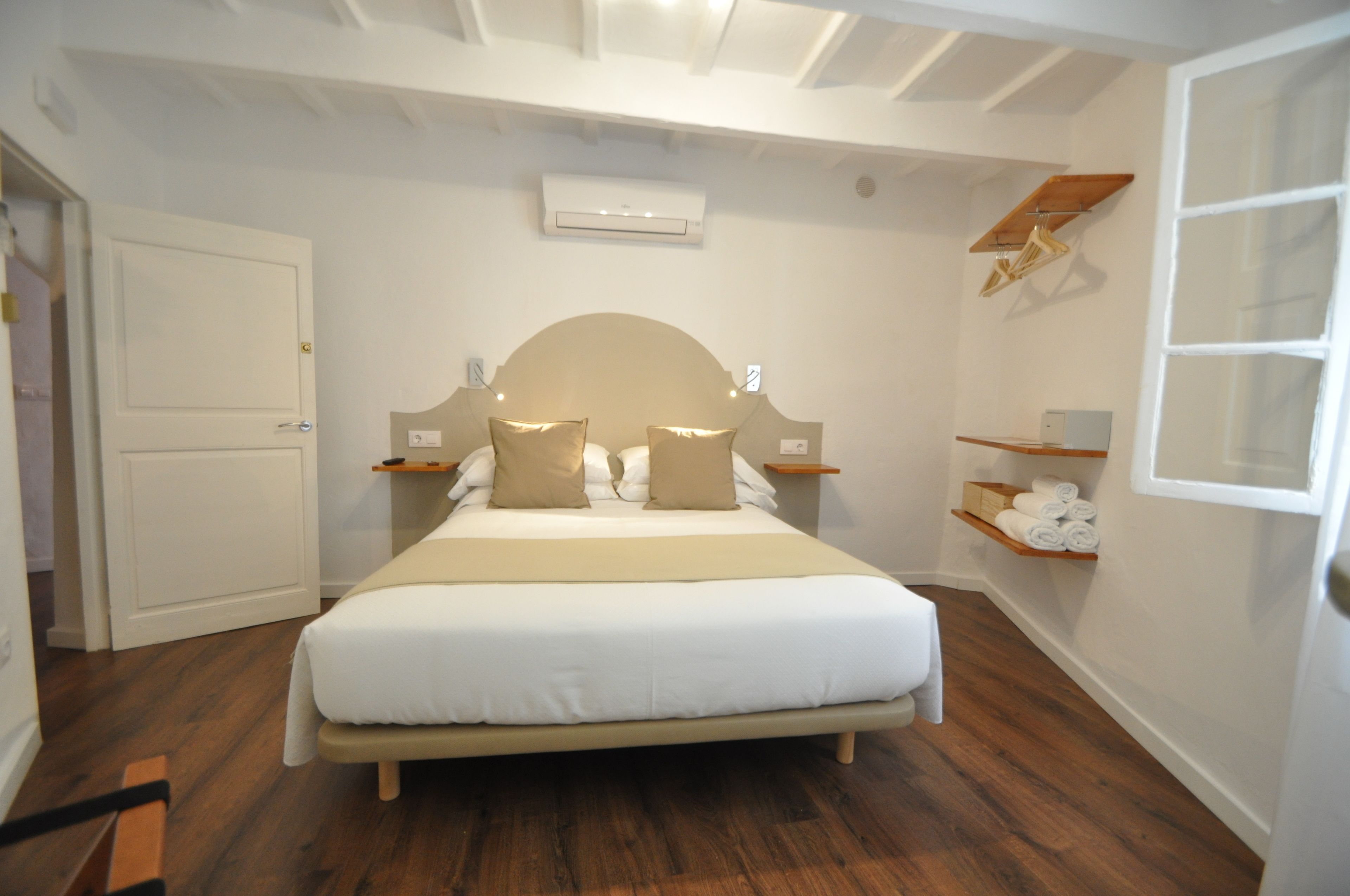 A neatly arranged bedroom with a bed, bedside tables, a hanging light fixture, and a built-in shelf with towels.