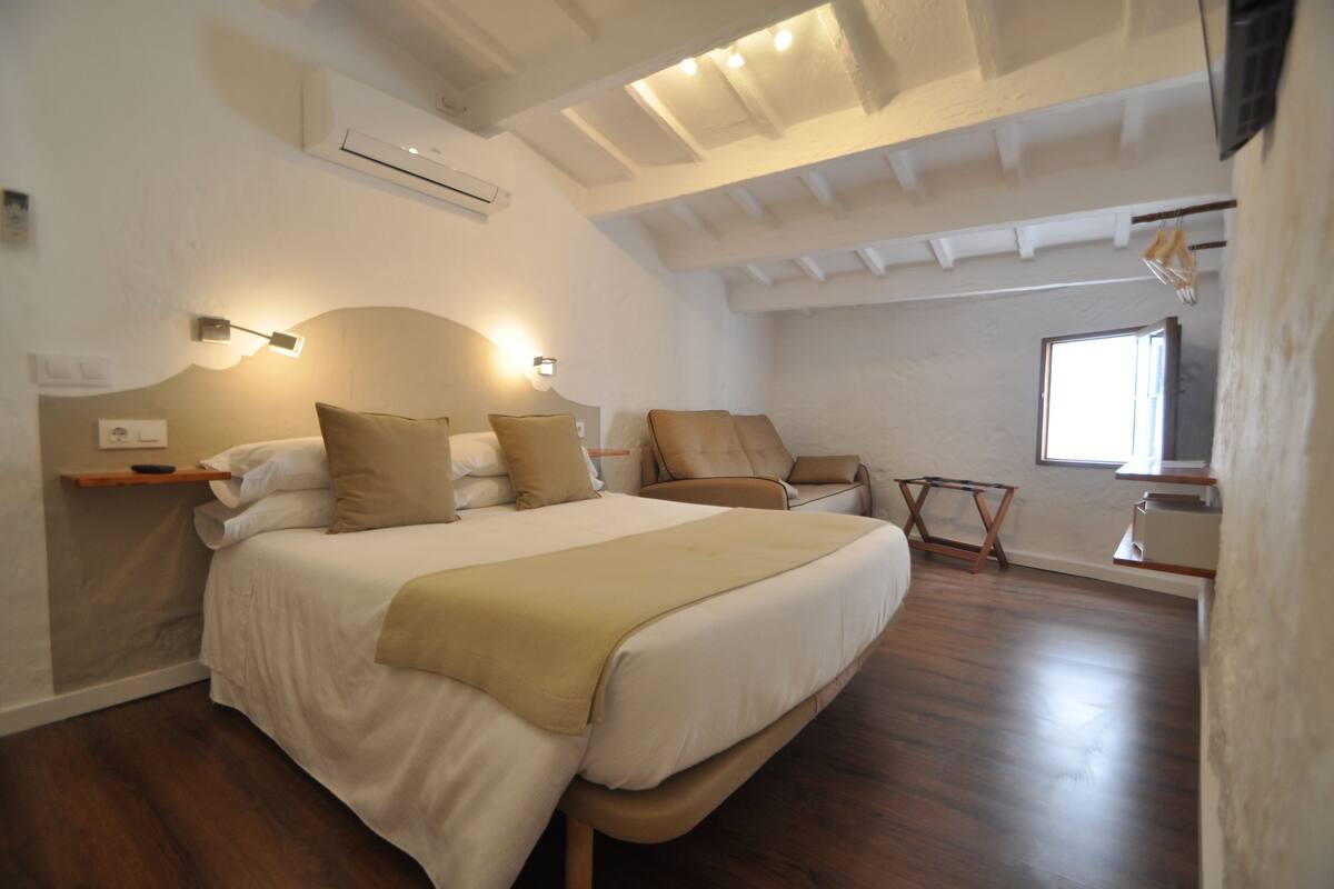 A bedroom with a large bed, a chair, a small table, and a window.