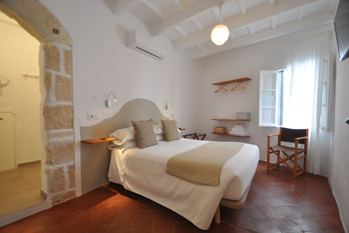 Un dormitorio con cama, una silla, un estante y una ventana.