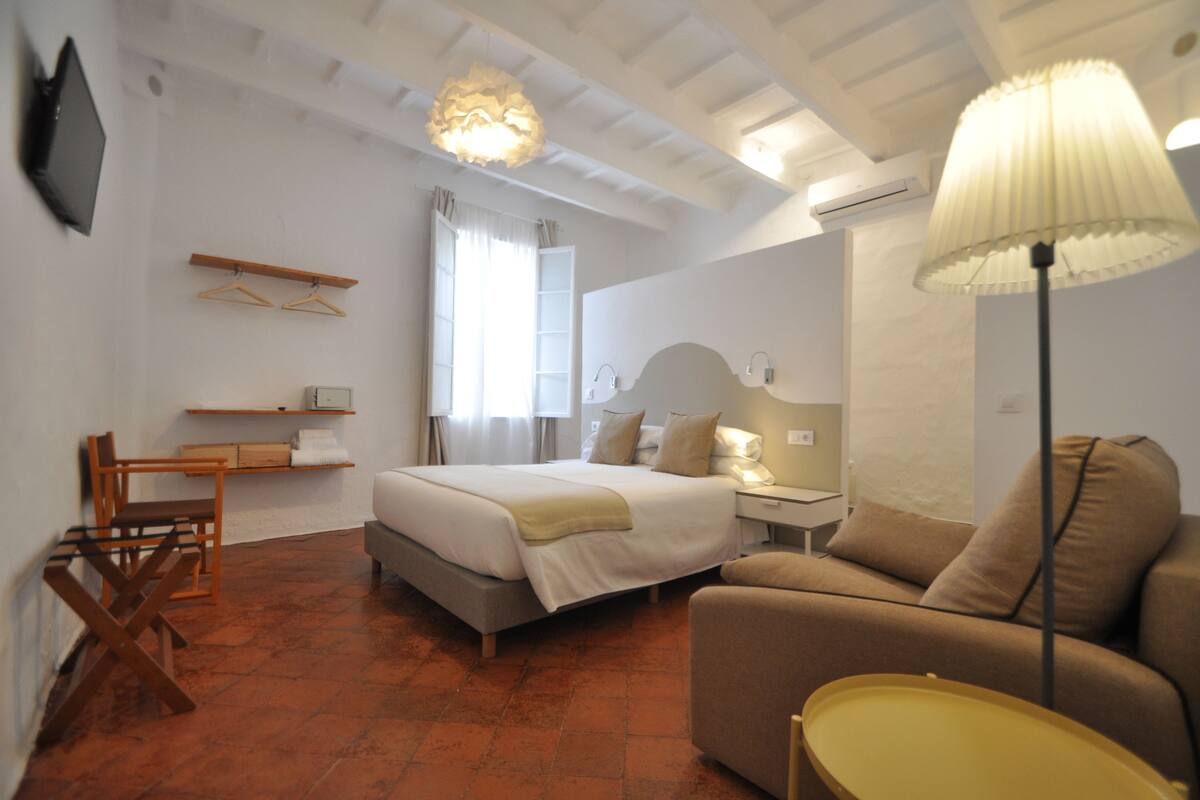 A bedroom with a bed, a bedside table, a lamp, a chair, and a TV mounted on the wall.
