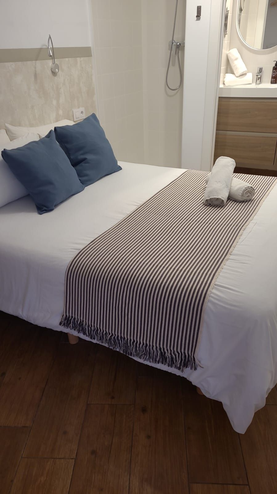 A neatly made bed with blue pillows, a striped blanket, and a wooden floor.