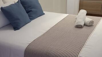 A neatly made bed with blue pillows, a striped blanket, and a wooden floor.