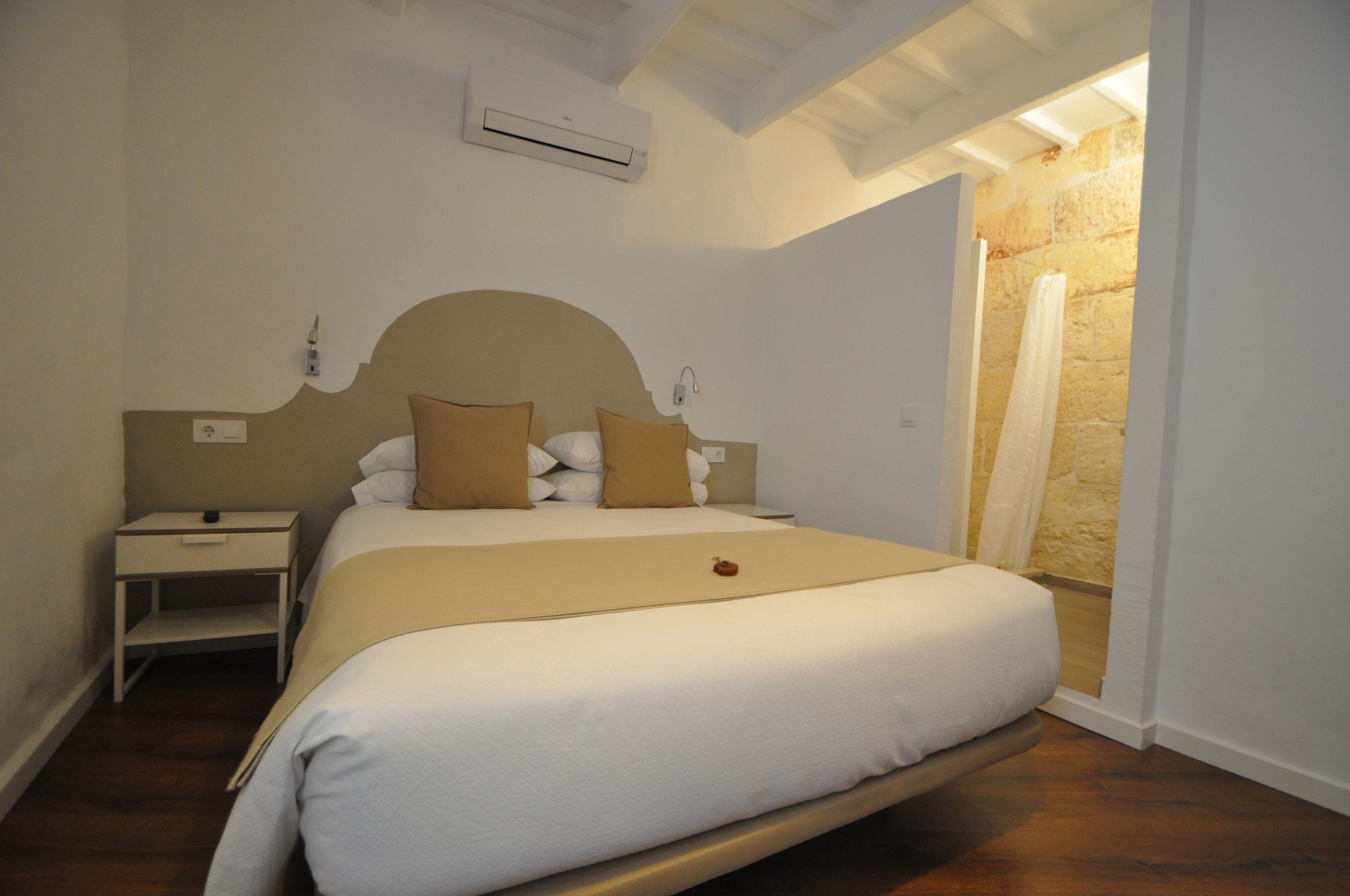 Un dormitorio ordenado con una cama grande, mesitas de noche y la puerta del baño a la vista.