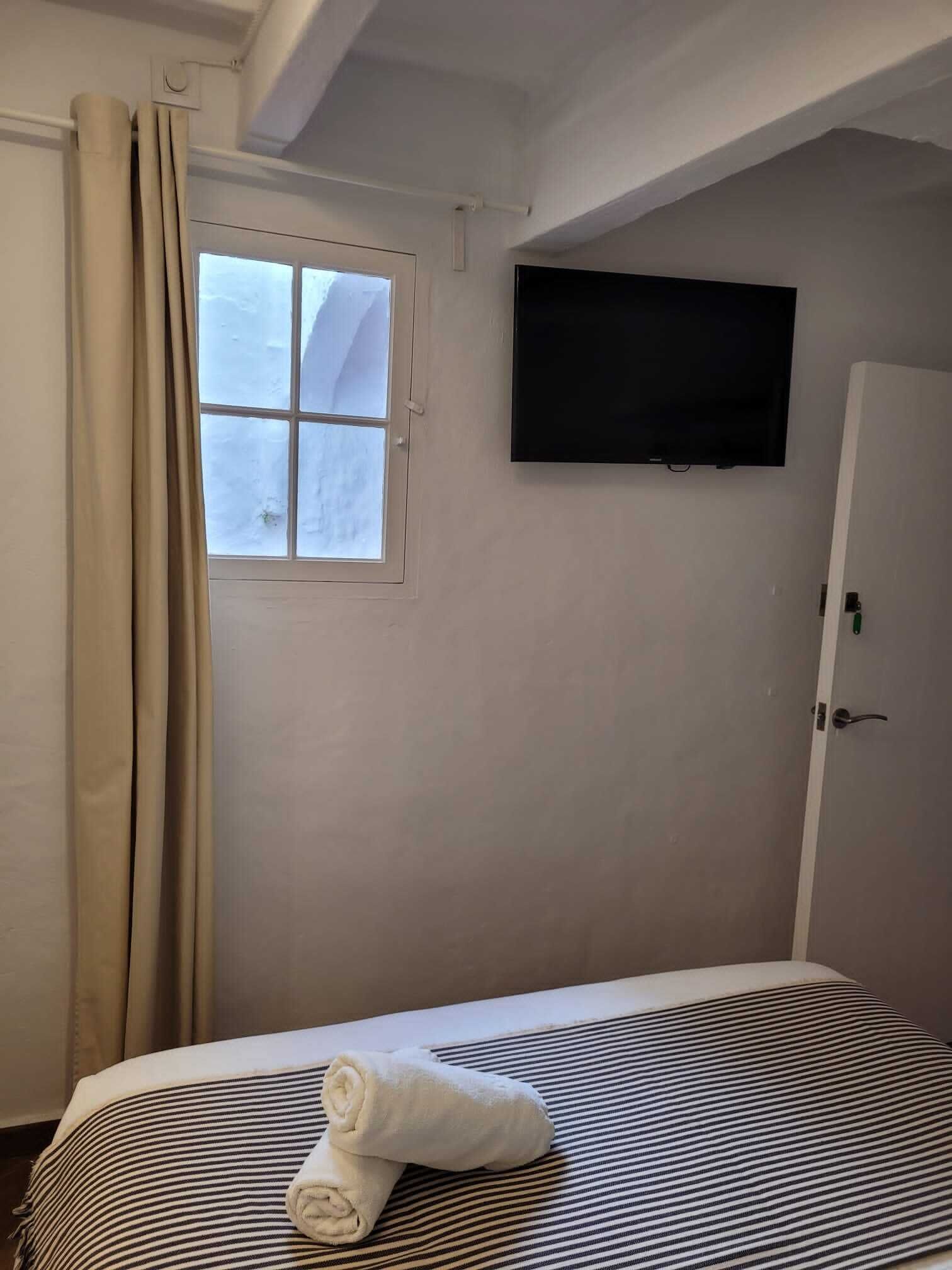 A bedroom with a bed, a window, a television, and a door.