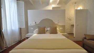Quarto de hotel com uma cama grande, mesa de cabeceira, sofá e espelho.