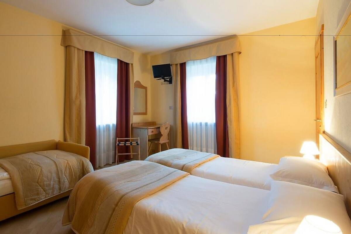 Habitación de hotel con dos camas, un escritorio, una silla y un televisor.