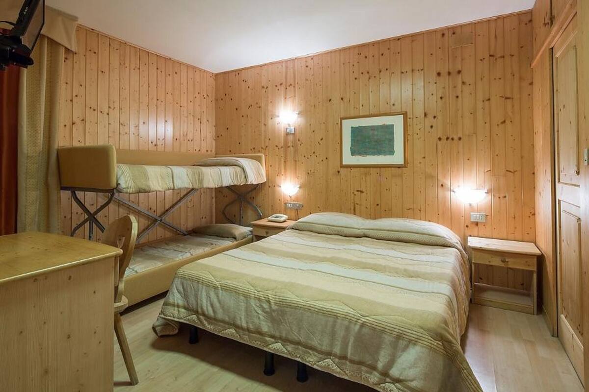 Una habitación con paneles de madera, una cama individual superpuesta, un escritorio y una mesita de noche con una lámpara.