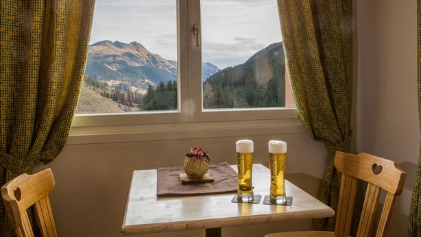 A table with two beer glasses and a decorative item by a window with a mountain view.