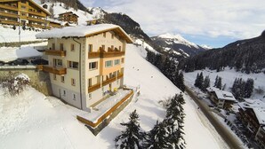 A hotel with a snow-covered roof and multiple balconies, surrounded by snow-covered mountains and trees.