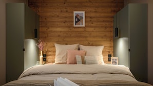 Ein modernes Schlafzimmer mit einer Holzwand, einem Bett mit vielen Kissen, einem Nachttisch mit einer Vase und einem Bilderrahmen sowie einer Schale Kekse auf dem Bett.