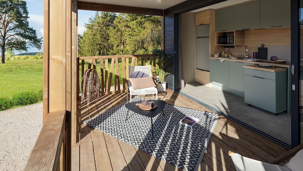 Eine Holzterrasse mit einem schwarz-weißen Teppich, einem weißen Stuhl und einem kleinen Tisch mit einem Buch.