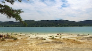 Ein Strand mit klarem Wasser, sandigem Ufer und Hügeln im Hintergrund.