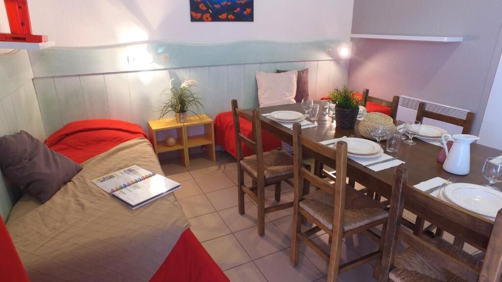A compact room with a bed, a dining table set for two, and a small side table with a plant.
