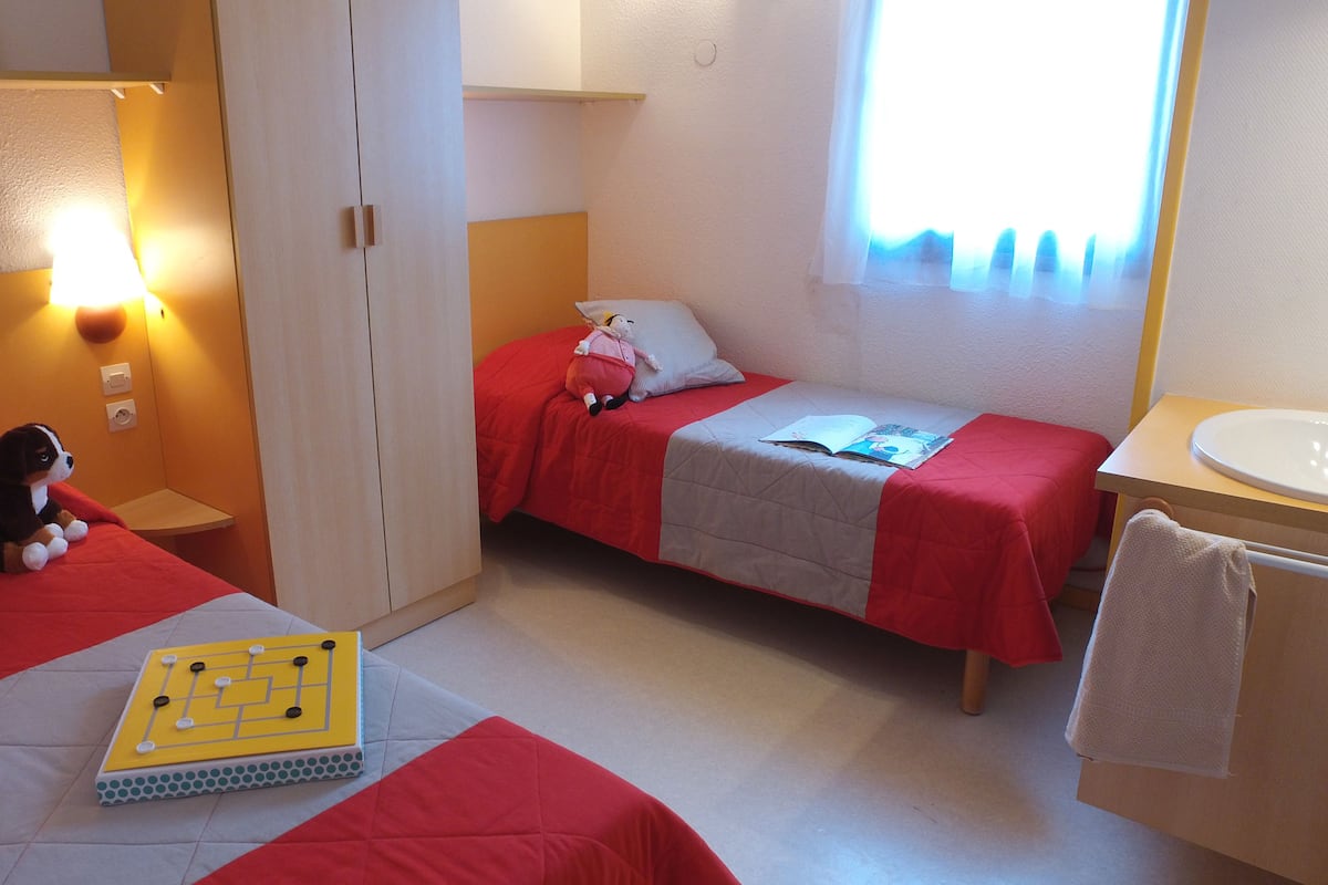 Habitación de hotel con dos camas, una mesita, una silla, un escritorio con lavamanos y una ventana con cortinas.