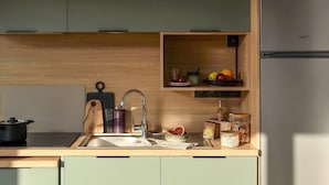 Eine moderne Küche mit Spüle, Herd und Kühlschrank. Holzschränke und ein Regal mit Früchten und Gläsern.