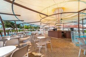 Un espace extérieur aménagé avec des tables et des chaises, protégé par un grand auvent, et offrant une vue sur une piscine.