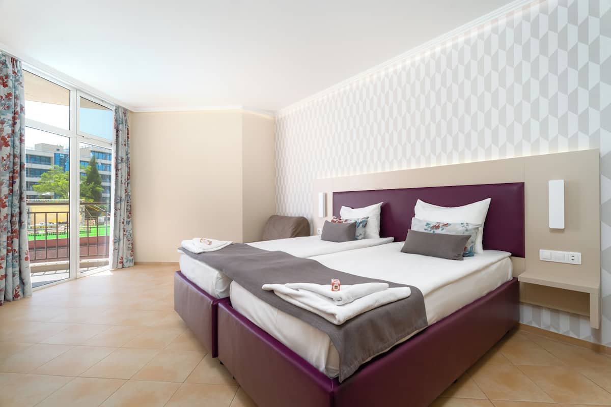 A modern hotel room with a large bed, a separate seating area, and a view of the outdoors.