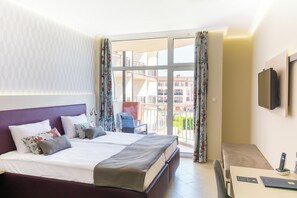 Une chambre d’hôtel équipée d’un lit, d’un bureau, d’une chaise, d’un balcon avec vue sur les bâtiments et d’un téléviseur fixé au mur.