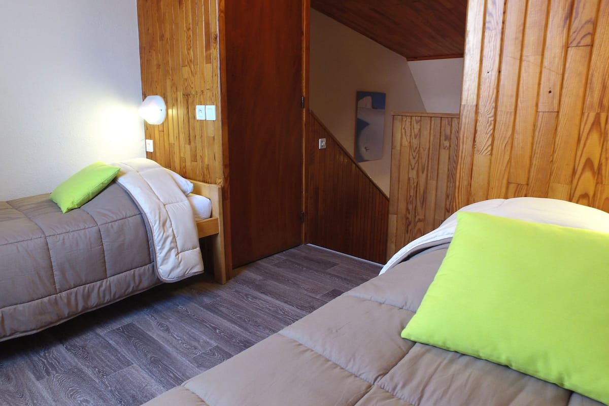 Ein kleiner, gemütlicher Raum mit zwei Einzelbetten, Holzwänden und einer Holztreppe.
