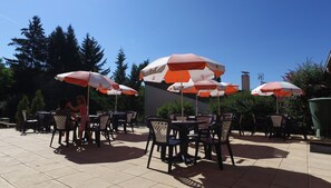 An outdoor patio area with multiple tables and chairs, some under umbrellas. - VVF Les Ecrins Champsaur, Saint Bonnet en Champsaur (Saint-Bonnet-en-Champsaur)