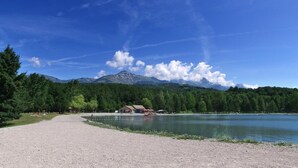 A lakeside view with a gravel path leading to a building with a red roof, surrounded by trees and mountains in the background. - VVF Les Ecrins Champsaur, Saint Bonnet en Champsaur (Saint-Bonnet-en-Champsaur)