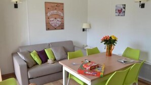 A living room with a grey sofa, green chairs, a wooden table, and a basketball on the floor. - VVF Les Ecrins Champsaur, Saint Bonnet en Champsaur (Saint-Bonnet-en-Champsaur)
