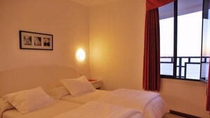 A hotel room with two beds, a nightstand, a wall-mounted light, a window with curtains, and a framed picture on the wall. - Balcon de Taurito (Mogan)