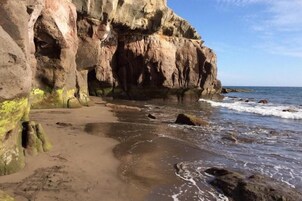 Una costa rocosa con una playa arenosa y olas rompiendo contra las rocas.
