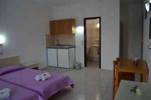A hotel room with a bed, a small table, a kitchenette, and a bathroom visible through an open door.