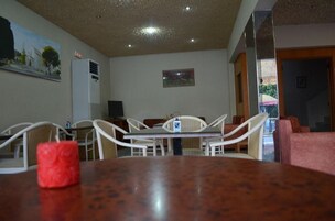 Uma área de refeições com uma mesa de madeira, cadeiras brancas, uma vela vermelha e um quadro na parede.