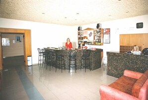 Zona de bar con mostrador, taburetes y una persona de pie detrás.