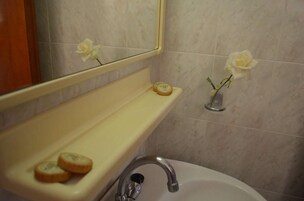 Um banheiro com pia, espelho e duas rosas brancas na parede.