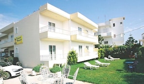 A multi-story building with balconies, a sign indicating a restaurant, outdoor seating with tables and chairs, and a car parked in front. - Kremasti Memories Apartments (Rhodes)