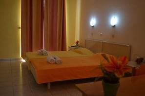 A hotel room with a bed, a nightstand with a lamp, and a vase with flowers. - Kremasti Memories Apartments (Rhodes)