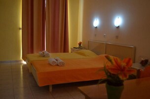 Una habitación de hotel con una cama, una mesita de noche, un jarrón con flores y dos lámparas de pared.
