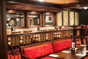Un restaurante con un banco tapizado en rojo, paneles de madera y vista a la calle a través de amplias ventanas.