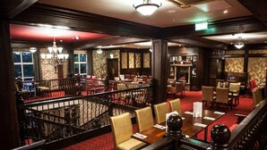 A hotel lobby with a red carpet, multiple dining areas with tables and chairs, and a staircase leading to an upper level. - Dillons Hotel (Letterkenny)