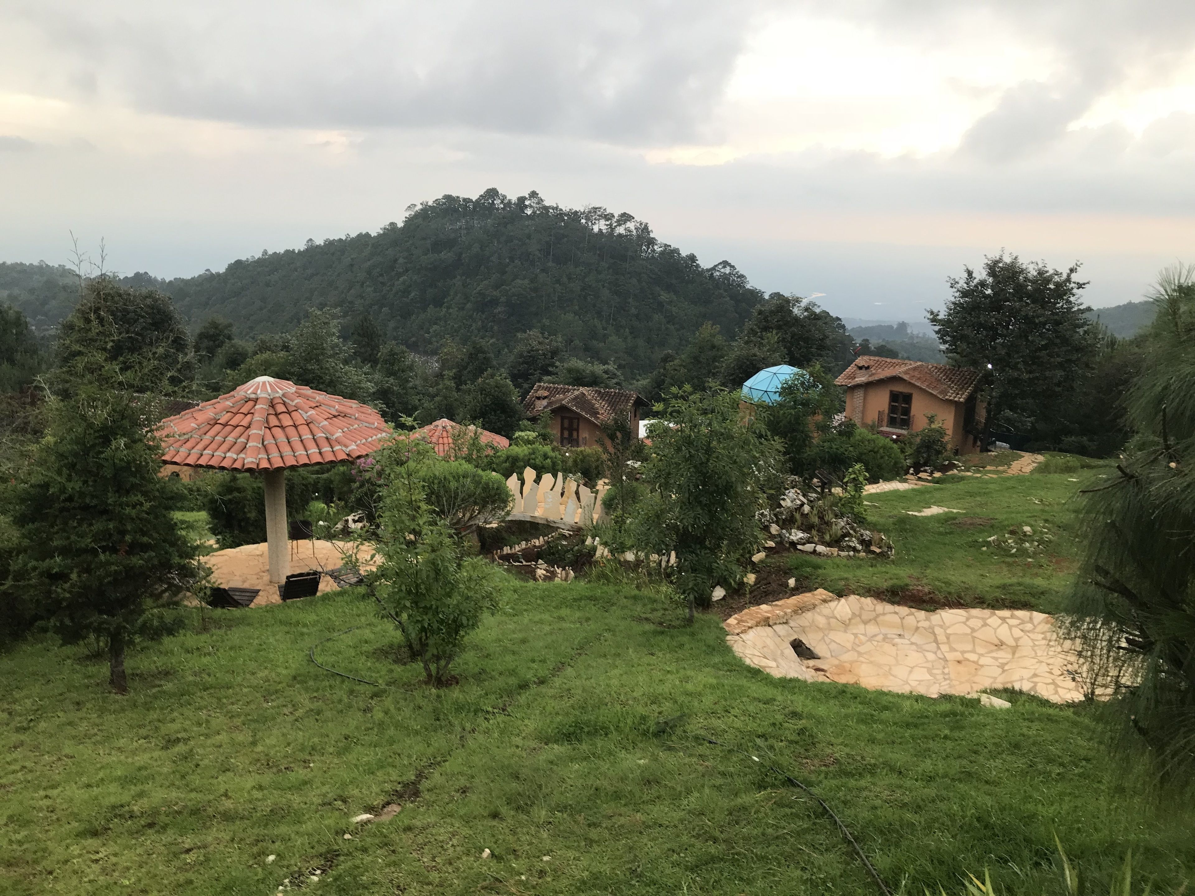 Un pueblo rural con casas tradicionales, un muro de piedra y montañas al fondo.