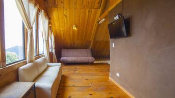 Une pièce chaleureuse avec un plafond en bois, un canapé, une table et un téléviseur fixé au mur.