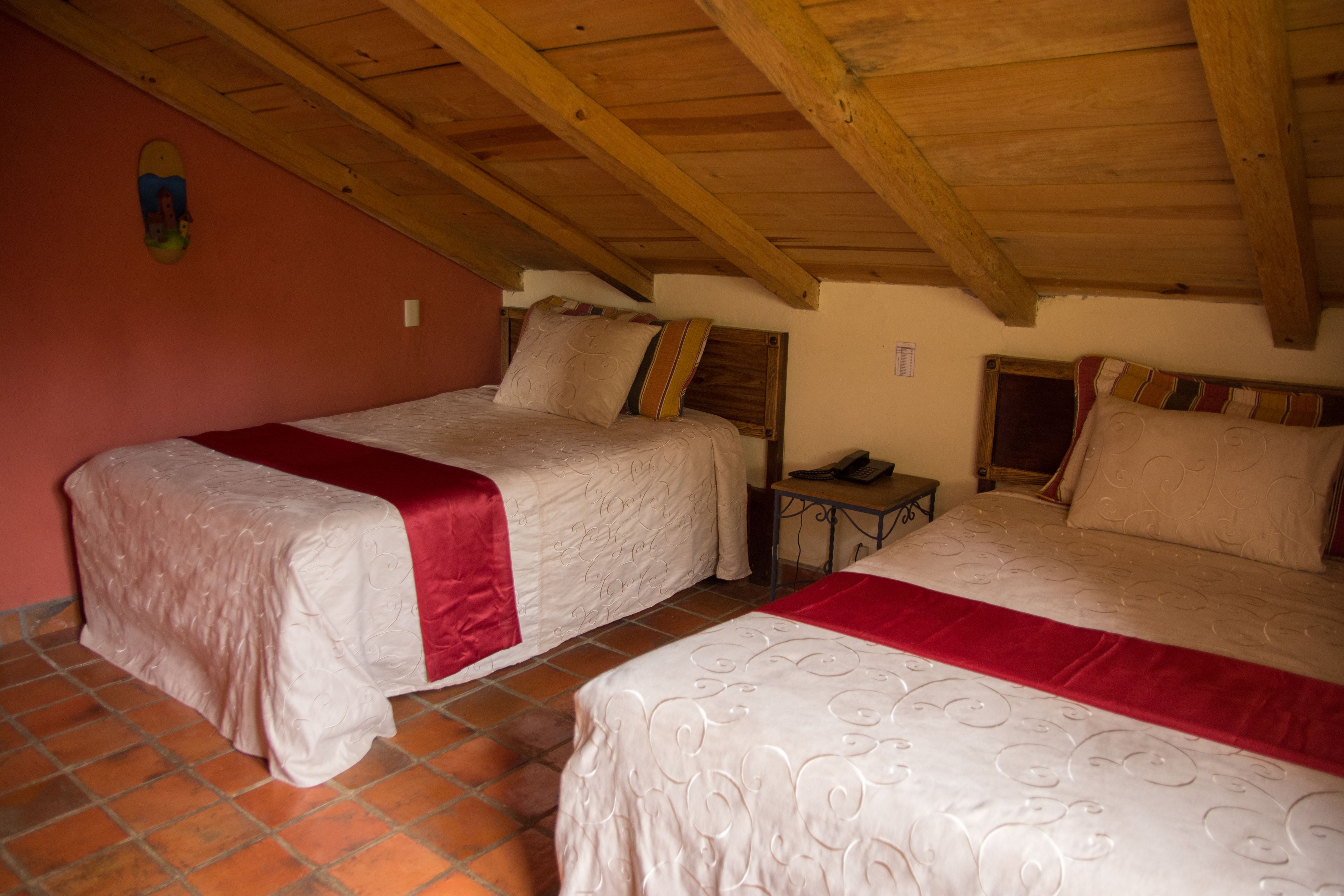 Een kamer met twee bedden, elk met een rode deken en witte lakens. De kamer heeft een houten plafond en een betegelde vloer.