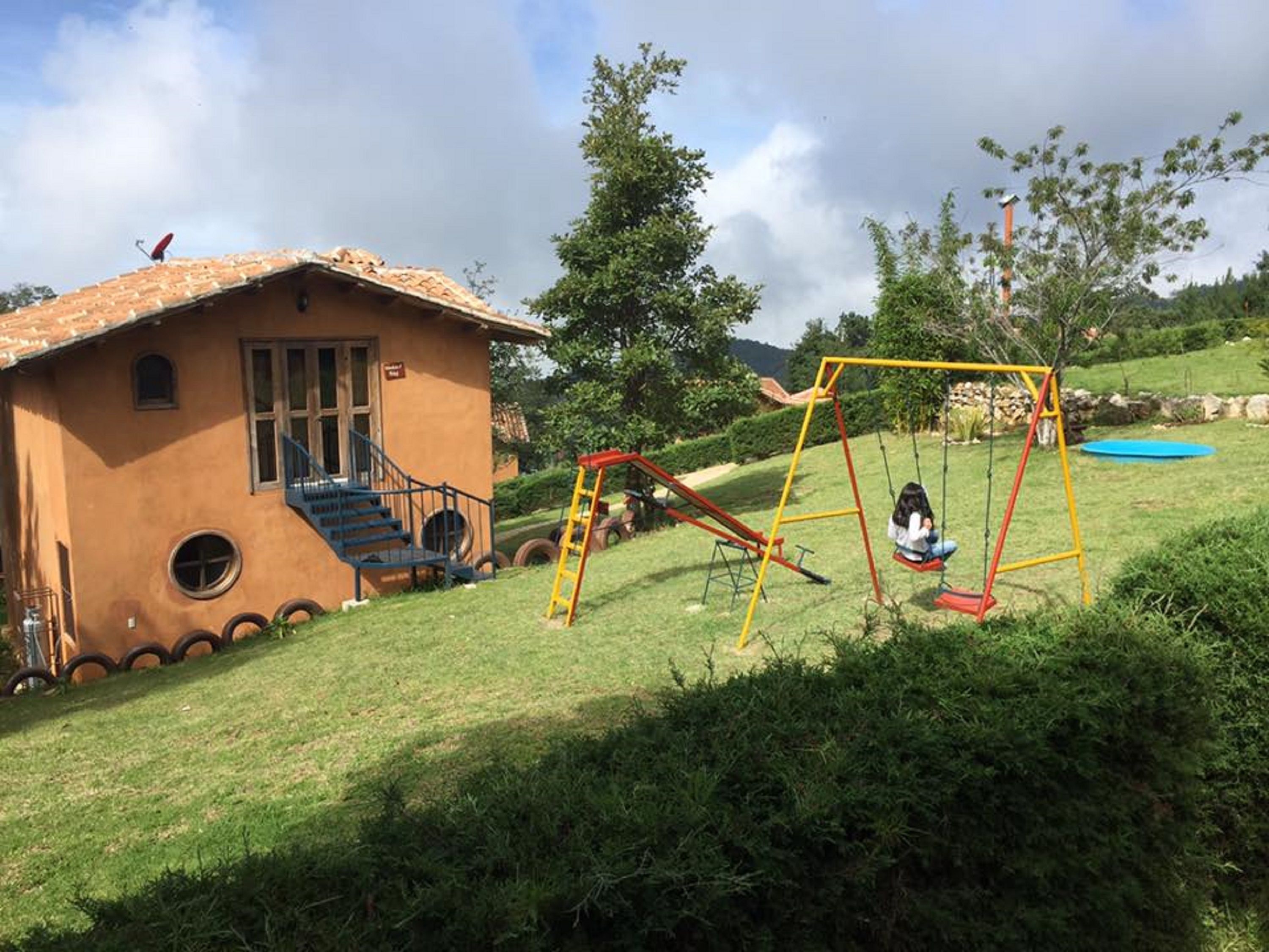 Una casa con una fachada singular, un columpio y un pequeño trampolín en un césped.