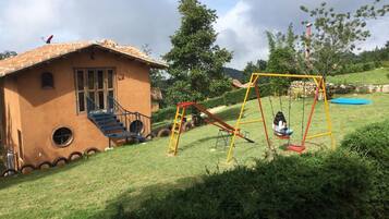 Una casa con una fachada singular, un columpio y un pequeño trampolín en un césped.