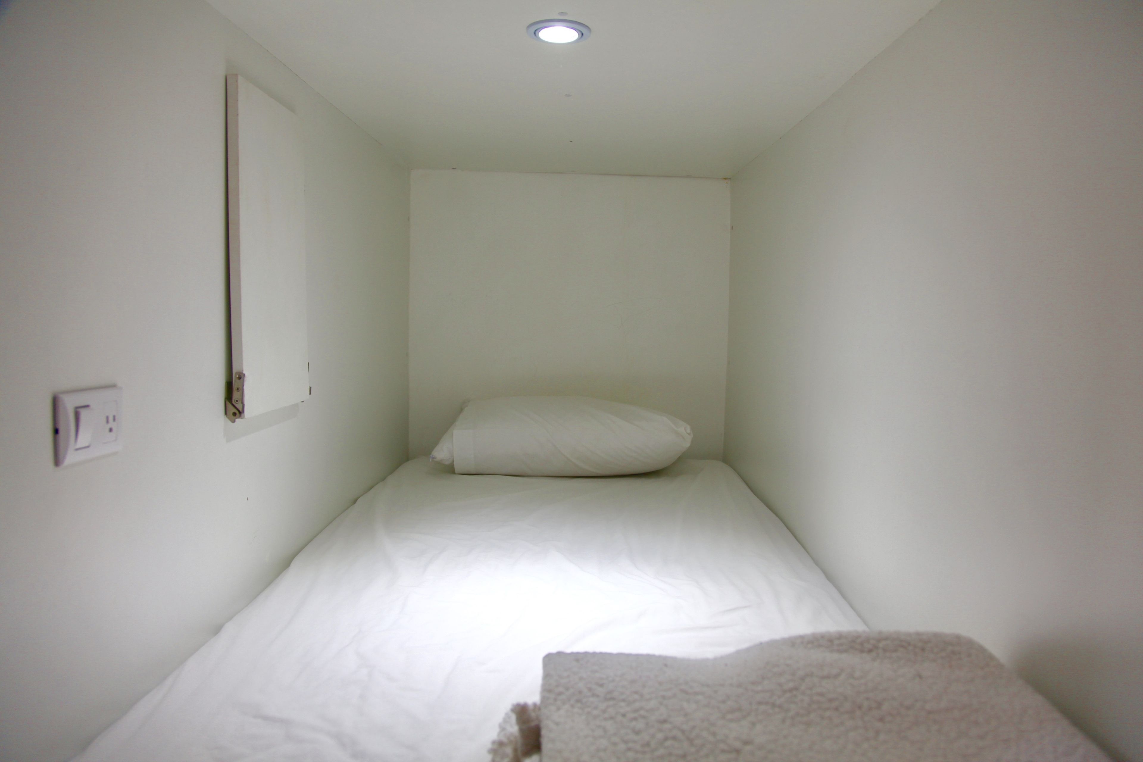 A small, single-bed room with white walls and a white bedspread.