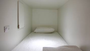 A small, single-bed room with white walls and a white bedspread.