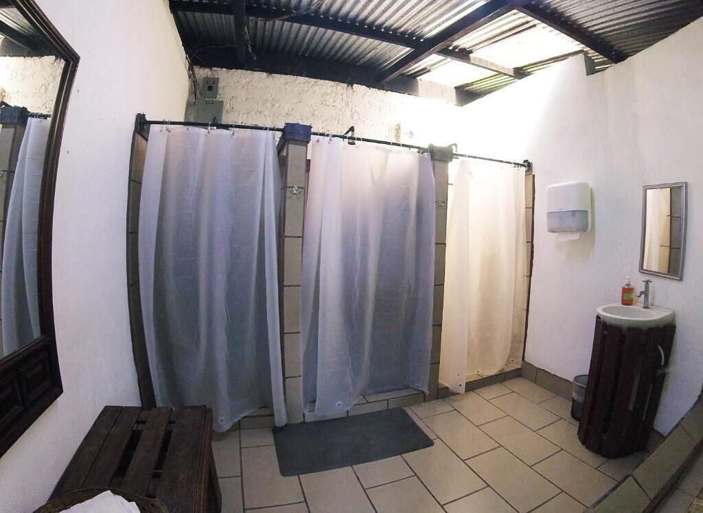 Kylpyhuoneessa on kaksi suihkuverhoa, pesuallas, peili ja puinen penkki.
